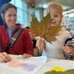 A mother looks at a young child holding an enormous leaf