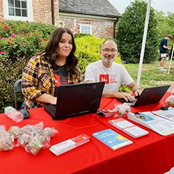 Two staff member smile behind a table and two laptops.