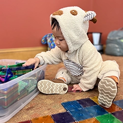 a young child in a teddy bear outfit plays with colorful toys
