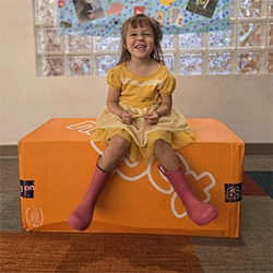 A young girl smiles at the camera while sitting on a orange cushion.