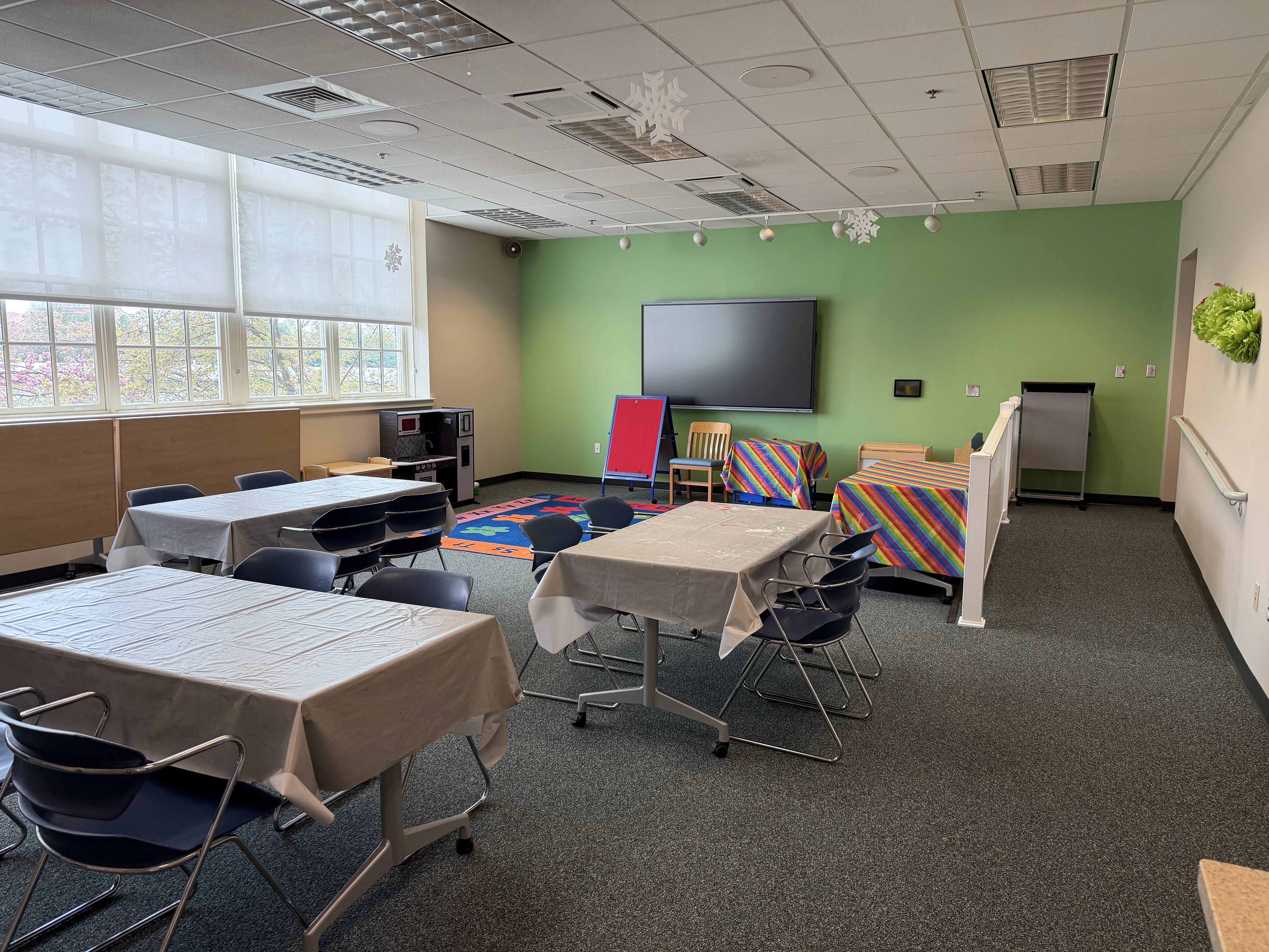 A view from just inside the doorway showing a brightly lit room with windows on the leftwall, tables and a green back wall