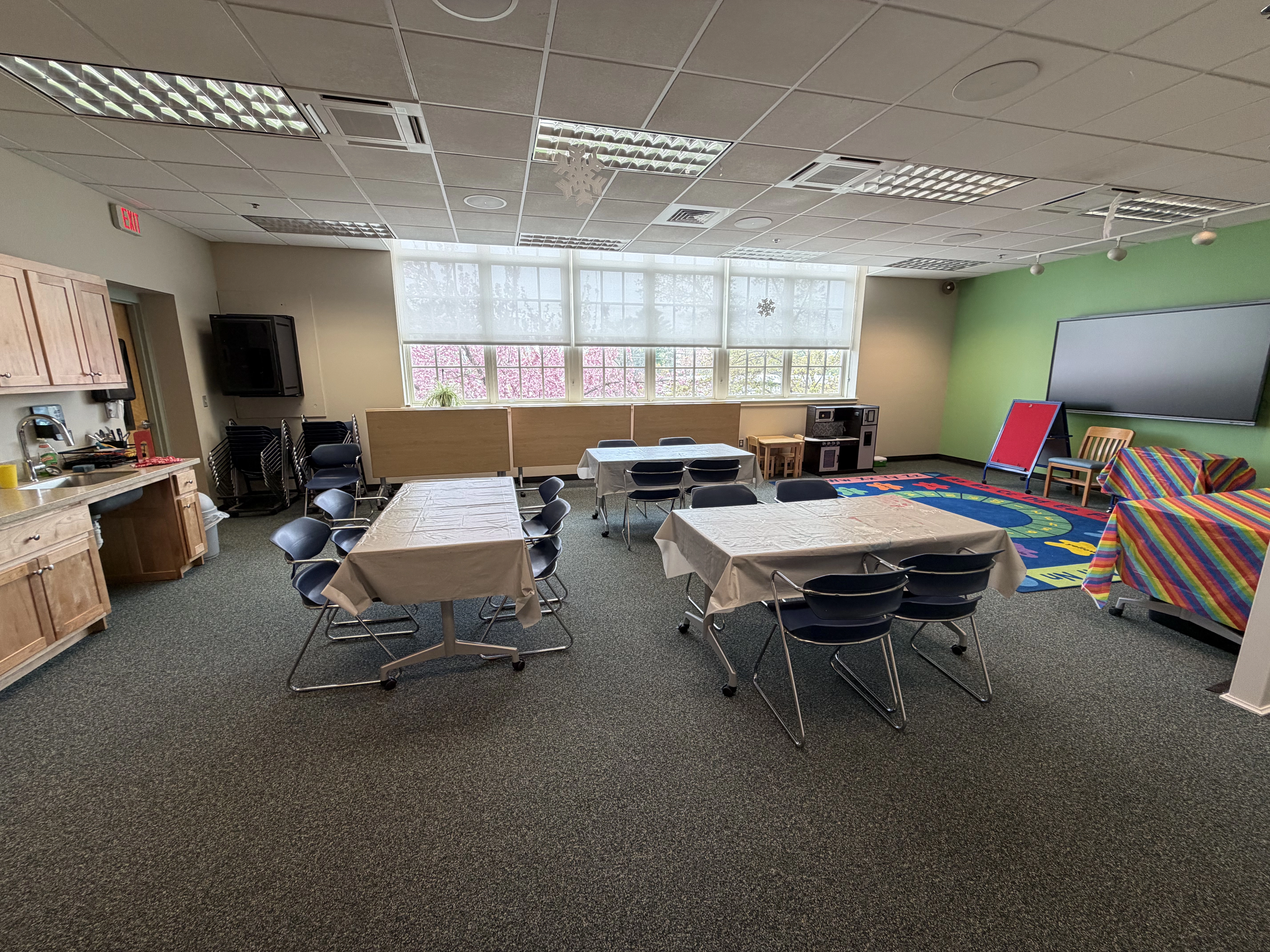 a view of the room from the right hand wall facing the windows with tables in the foreground