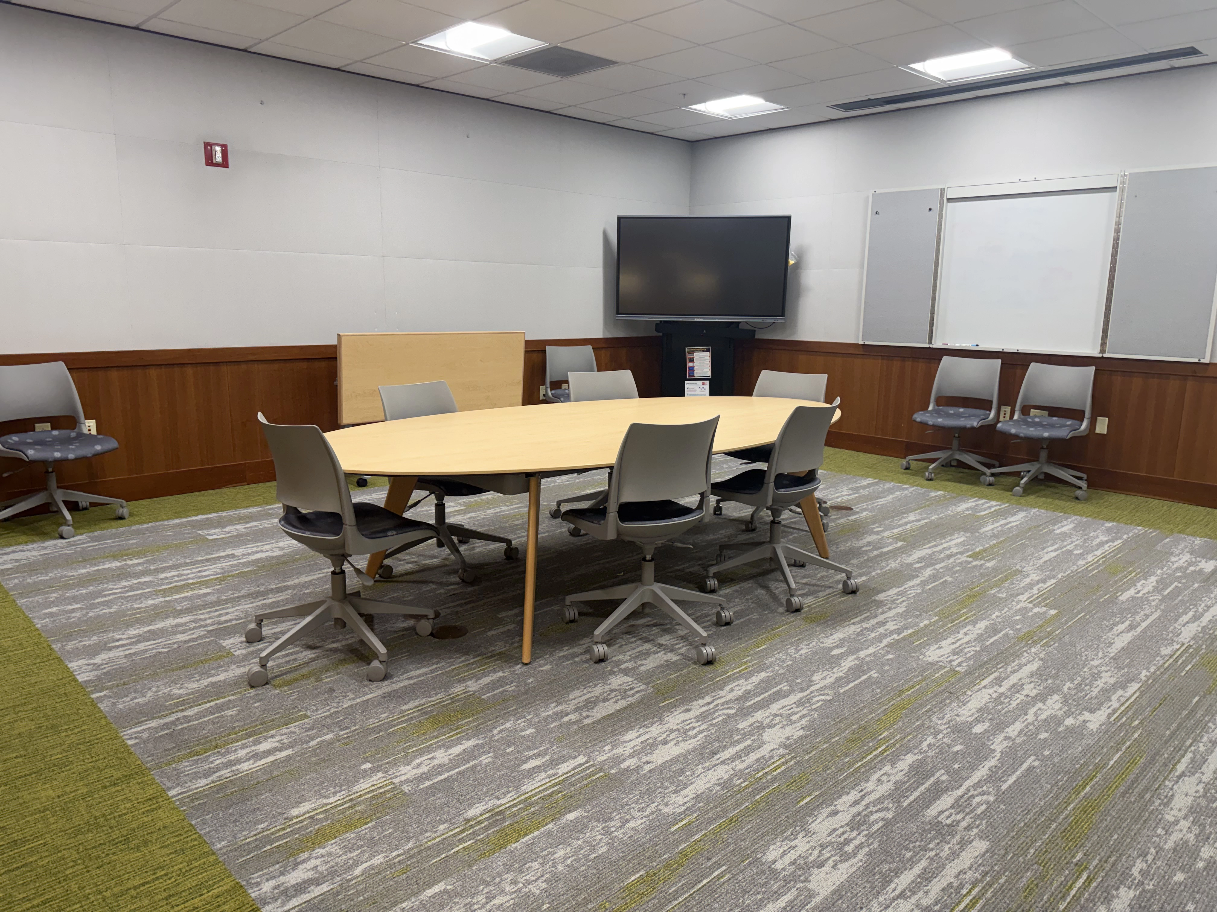 A view of the inside left corner of the room showing a large oval table and chairs with a movable large monitor display