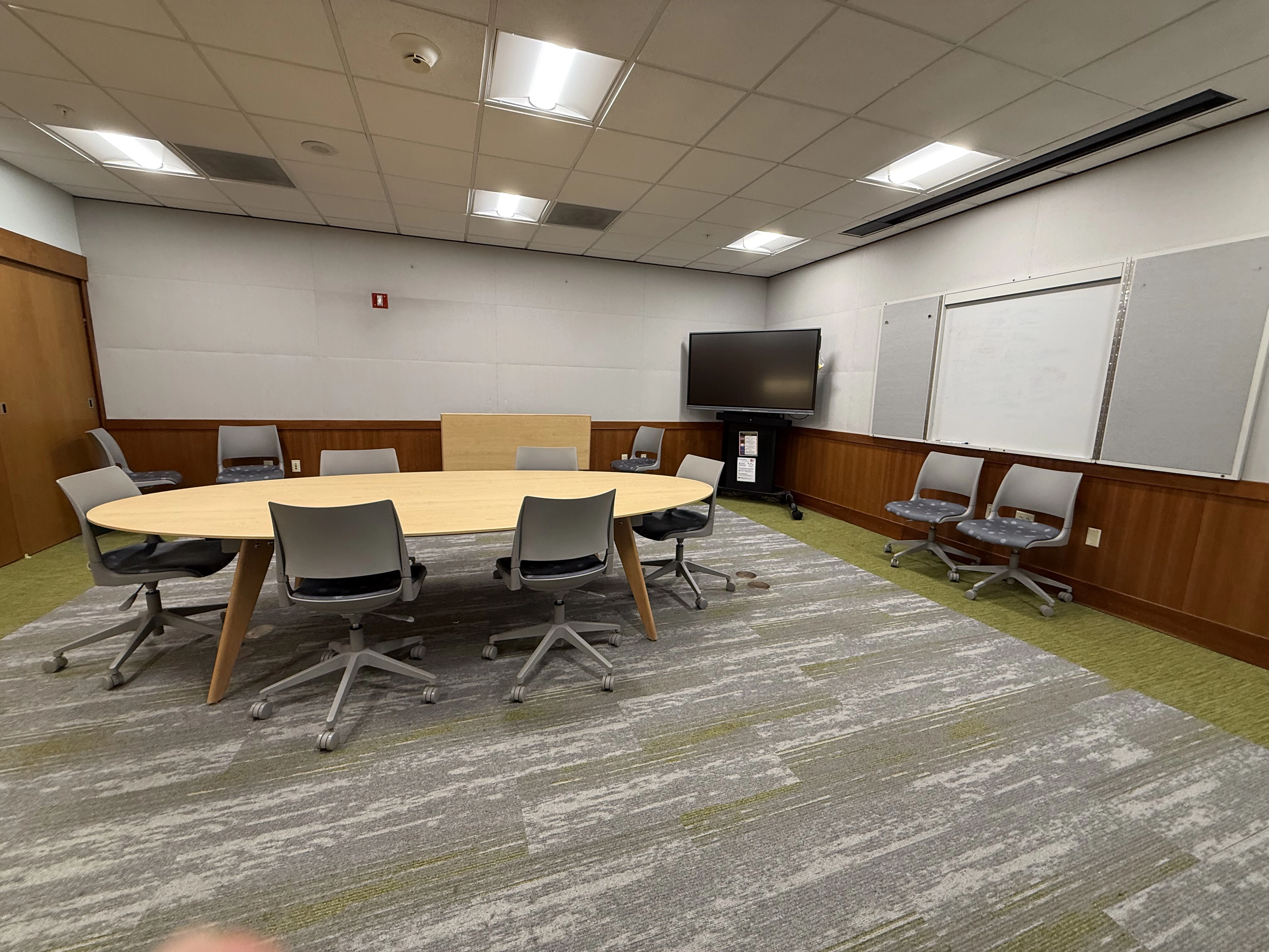 a view of the Trust room from mid-way in the room showing the large oval table, chairs and the large movable monitor