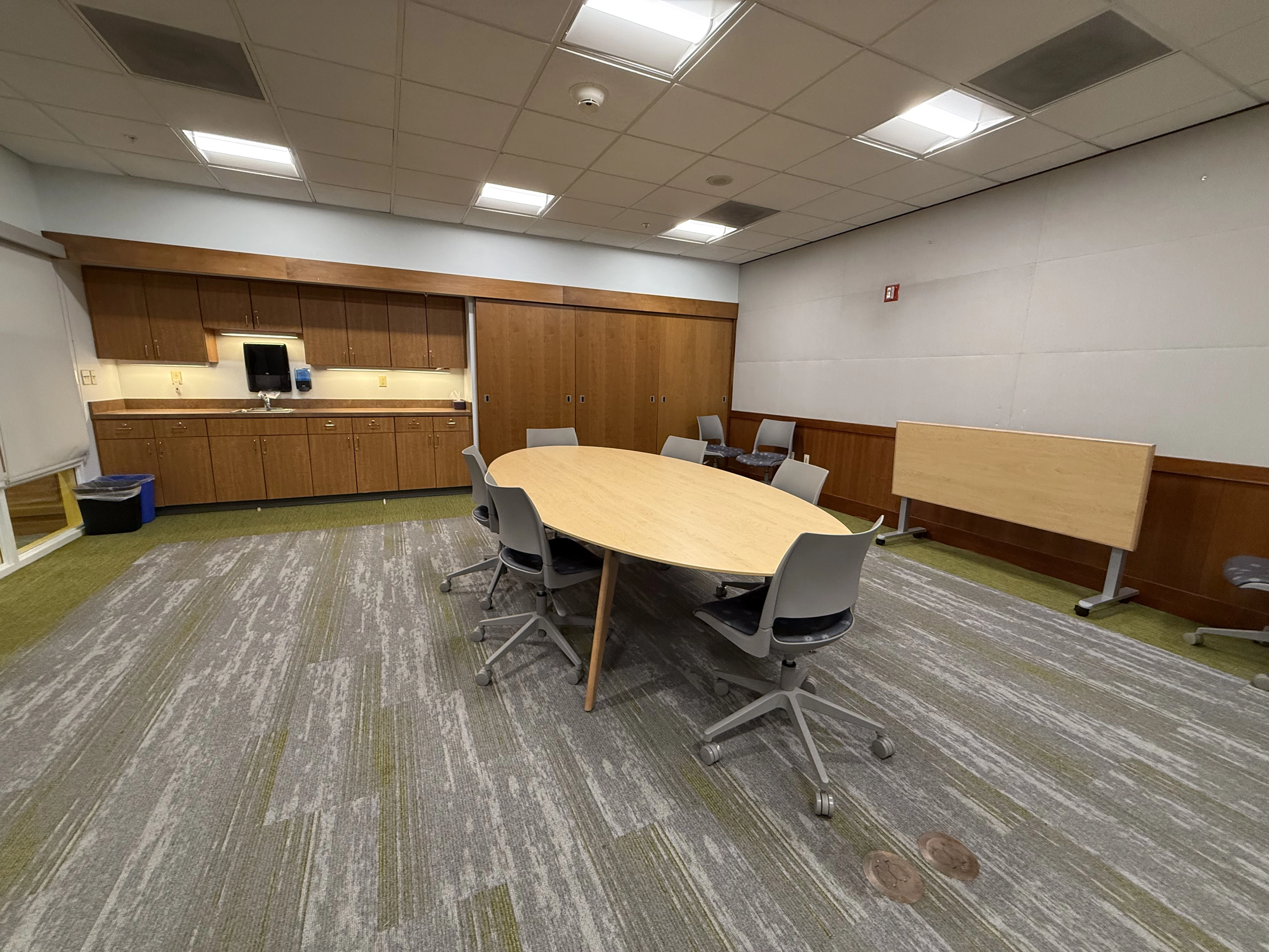 A view from the right hand wall of the room facing the kitchen area beyond the large oval table and chairs