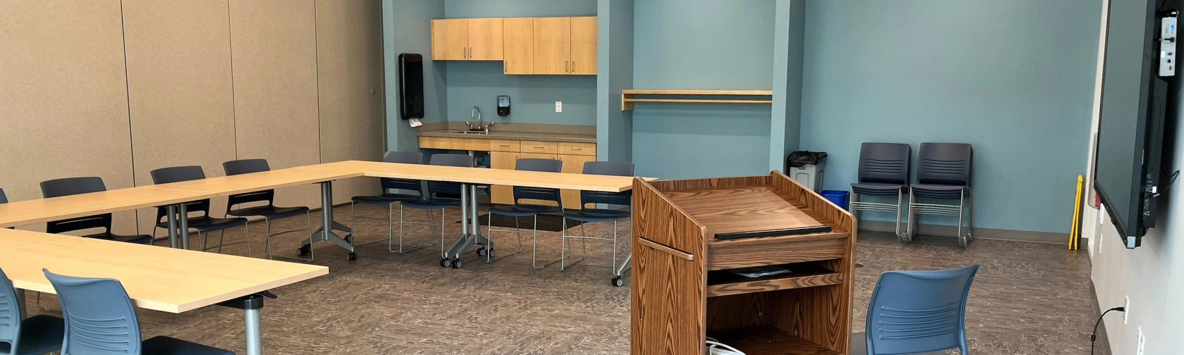 Meeting Room A showing a brightly lit space with kitchen area, tables, chairs and a podium