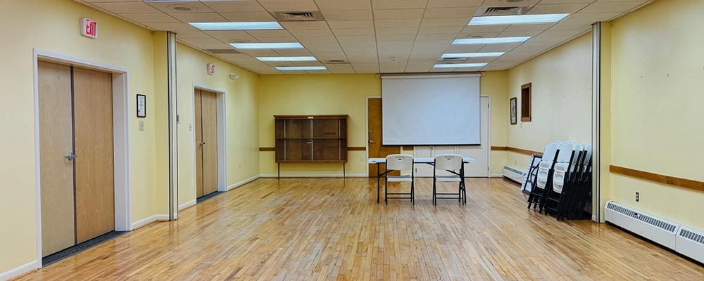 A large brightly lit space with a projector screen, table, chairs and yellow walls