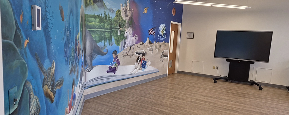 a view of the room with a brightly colored mural on the left hand wall and a movable display on the right