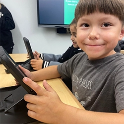 A child smiles at the camera while holding a tablet