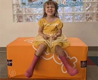 A young girl smiles at the viewer while sitting on an orange cushion